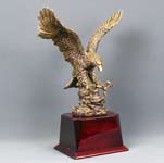 This is a image of a large antique gold eagle on a redwood piano finish square base